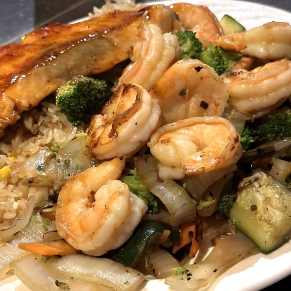 Hibachi salmon and shrimp with fried rice and mixed vegetables, including broccoli, zucchini, and onions.