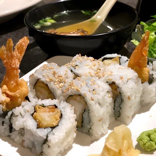 Shrimp tempura sushi rolls with sesame seeds, ginger, wasabi, and a bowl of soup.