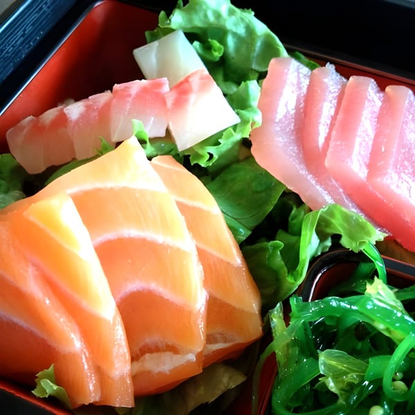 Assorted sashimi slices, including salmon and tuna, served with green lettuce and seaweed salad.