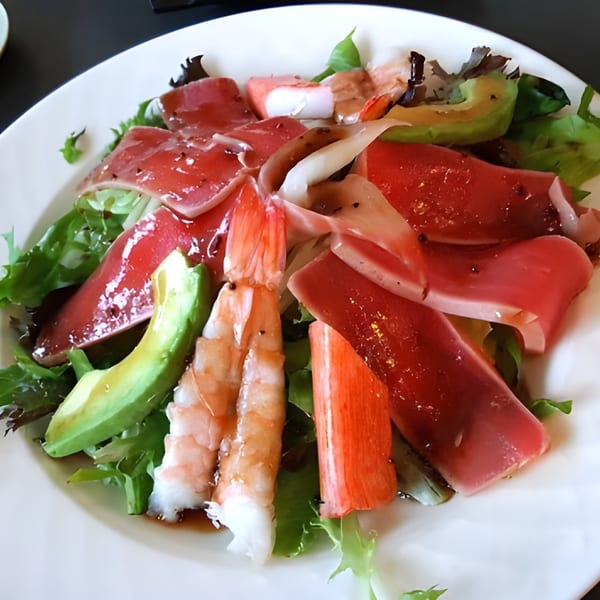A vibrant Japanese salad with tuna, shrimp, crab, avocado, and mixed greens on a white plate.