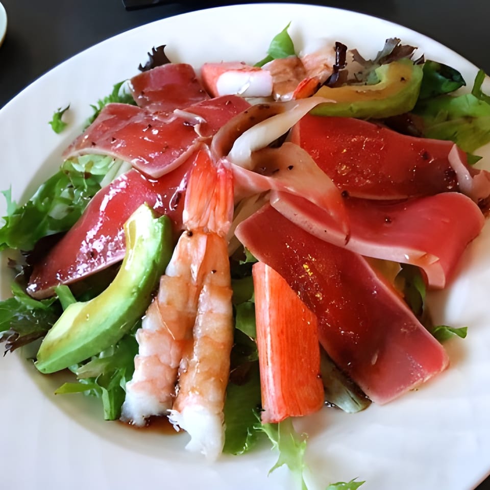 A vibrant Japanese salad with tuna, shrimp, crab, avocado, and mixed greens on a white plate.